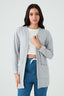 Woman wearing a light gray cardigan over a white top and blue jeans on a light gray background
