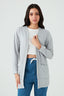 Woman wearing a light gray cardigan over a white top and blue jeans on a light gray background